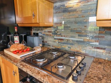 A kitchen countertop with a gas stove a bottle of wine two wine glasses bread tomatoes and a toaster at Stag Lodge Holiday Retreat Whitby