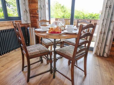 A wooden dining table with four chairs set with crockery and pastries in a room with wooden floors and floral curtains at Stag Lodge Holiday Retreat Whitby