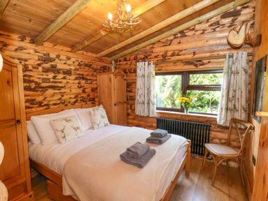 A bedroom with a double bed two wooden wardrobes a window with curtains and a wooden chair at Stag Lodge Holiday Retreat Whitby