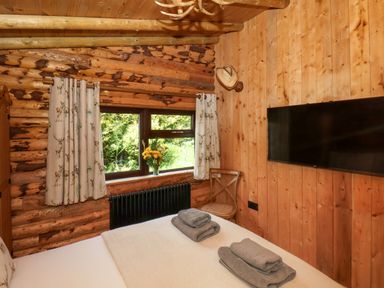 A bedroom with a bed towels on the bed a chair a vase with flowers on the windowsill and a wall-mounted TV at Stag Lodge Holiday Retreat Whitby