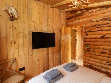 A bedroom with wooden walls a mounted television a wooden chair and folded towels on the bed at Stag Lodge Holiday Retreat in Whitby