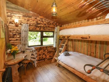 A small bedroom with wooden bunk beds a wooden desk with flowers a chair and a window at Stag Lodge Holiday Retreat in Whitby