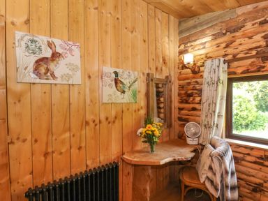 A wooden corner desk with a vase of flowers and a small fan near a window with curtains in a log cabin at Stag Lodge Holiday Retreat Whitby