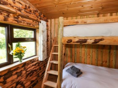 A wooden bunk bed next to a window with flowers on the windowsill in a log cabin bedroom at Stag Lodge Holiday Retreat Whitby