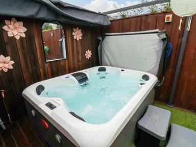 An outdoor hot tub with water jets surrounded by wooden paneling and decorated with flower ornaments at Stag Lodge Holiday Retreat Whitby