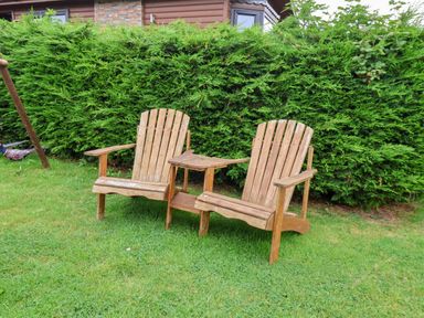A pair of wooden chairs connected by a small table on grass in front of a hedge at Stag Lodge Holiday Retreat Whitby