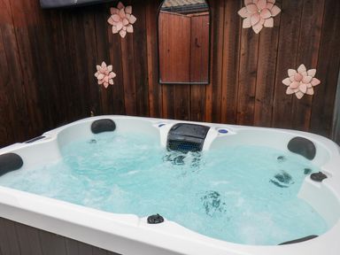 A hot tub with water jets against a wooden wall with decorative flowers and a mirror at Stag Lodge Holiday Retreat Whitby
