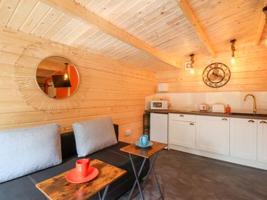 A kitchenette with white cabinets a sink and microwave next to a black couch with gray cushions and wooden side tables at Log Cabin - Amber Glow in Glastonbury