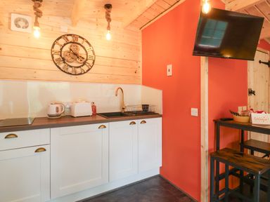 A kitchen area with white cabinets a wall clock a sink and a mounted television at Log Cabin - Amber Glow in Glastonbury