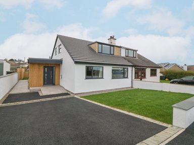 A white house with a black roof a wooden door and a green lawn at 11 Capel Farm in Trearddur Bay