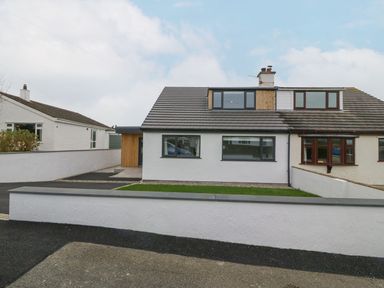 A white semi detached house with a driveway and a lawn in front at 11 Capel Farm in Trearddur Bay