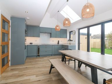 A kitchen with blue cabinets wooden dining table and bench under pendant lights at 11 Capel Farm in Trearddur Bay