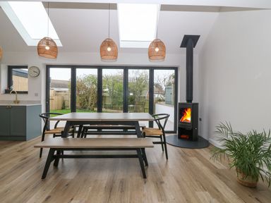 A dining area with a wooden table benches chairs and a fireplace at 11 Capel Farm in Trearddur Bay