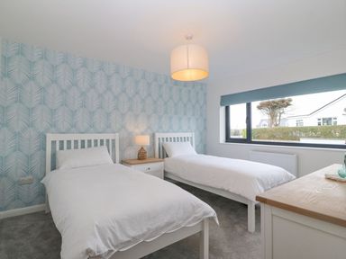 A bedroom with two single beds a nightstand lamp and a window at 11 Capel Farm in Trearddur Bay
