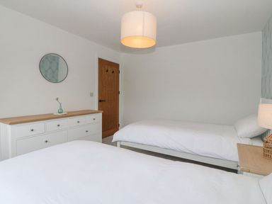 A bedroom with two single beds a white dresser a wooden door and a round mirror at 11 Capel Farm in Trearddur Bay