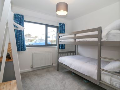 A bedroom with a bunk bed and a window with blue curtains at 11 Capel Farm in Trearddur Bay