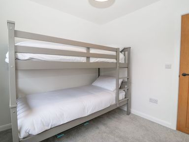 A bedroom with a gray bunk bed with white bedding and gray carpet at 11 Capel Farm in Trearddur Bay