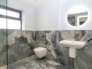 A bathroom with wall-mounted toilet and sink and a round mirror above the sink at 11 Capel Farm in Trearddur Bay