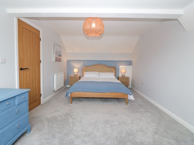 A bedroom with a bed lamps on bedside tables a blue dresser and a wooden door at 11 Capel Farm in Trearddur Bay