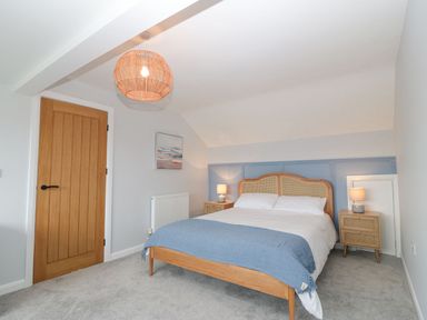 A bedroom with a double bed with a blue throw and two bedside tables with lamps at 11 Capel Farm in Trearddur Bay