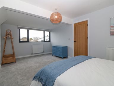 A bedroom with a bed covered in white and blue bedding a blue chest of drawers a wooden door and a window at 11 Capel Farm in Trearddur Bay