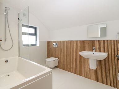 A bathroom with a bathtub shower toilet and sink with wood paneling on the wall at 11 Capel Farm in Trearddur Bay