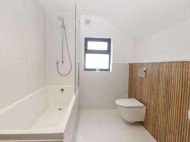 A bathroom with a bathtub shower combination and a wall-mounted toilet with wooden paneling at 11 Capel Farm in Trearddur Bay