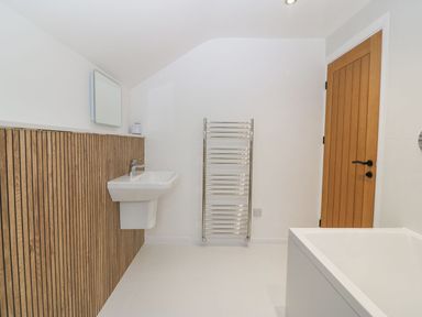 A bathroom with a wall-mounted sink wooden paneling a towel radiator a wooden door and a bathtub at 11 Capel Farm in Trearddur Bay