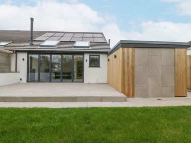 A backyard with green grass a tiled patio and a modern building with solar panels and skylights at 11 Capel Farm in Trearddur Bay