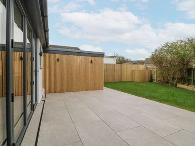 A backyard with tiled patio adjacent to a grassy lawn and wooden fencing at 11 Capel Farm in Trearddur Bay
