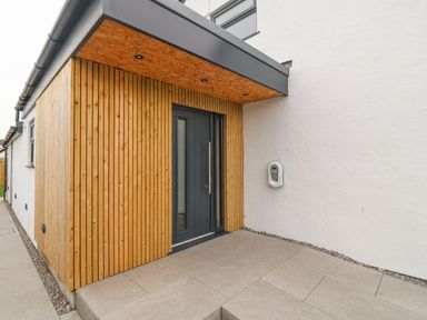 An entrance area with a wooden panelled wall and a dark grey door at 11 Capel Farm in Trearddur Bay
