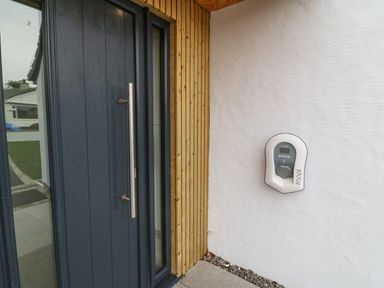 A dark blue front door with a metal handle next to a wall with a zappi electric car charger at 11 Capel Farm in Trearddur Bay