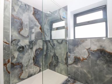 A shower area with patterned stone walls and a glass screen by a window at 11 Capel Farm in Trearddur Bay