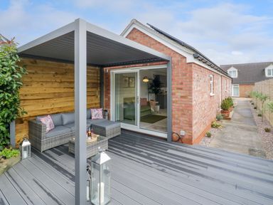 A covered patio with outdoor sofa and table beside a brick house at The Croft in Shipston-On-Stour