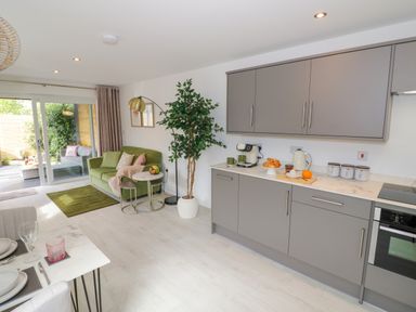 An open-plan kitchen and living area with grey cabinets, a green sofa, a potted plant, and a dining table at The Croft in Shipston-On-Stour