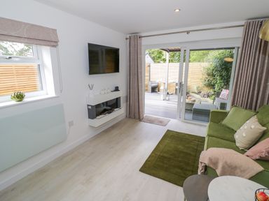 A living room with a green sofa a wall-mounted television and sliding glass doors leading to a patio at The Croft in Shipston-On-Stour