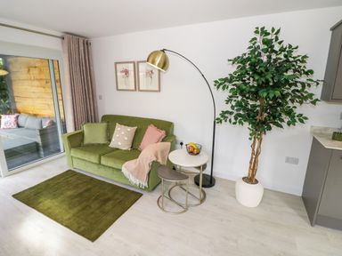 A living room with a green sofa pillows a floor lamp a potted plant and a small table at The Croft in Shipston-On-Stour
