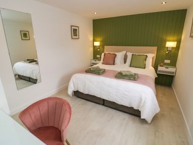 A bedroom with a double bed green and pink pillows bedside shelves a wall mirror and a pink chair at The Croft in Shipston-On-Stour