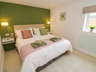 A bedroom with a double bed green accent wall wall-mounted bedside tables and window at The Croft in Shipston-On-Stour
