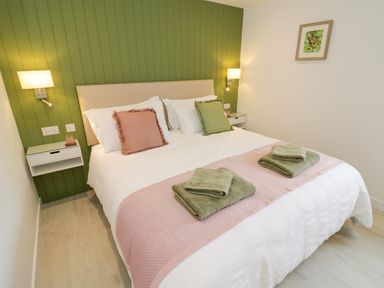 A bedroom with a double bed with green and pink pillows and folded towels on a pink runner at The Croft in Shipston-On-Stour