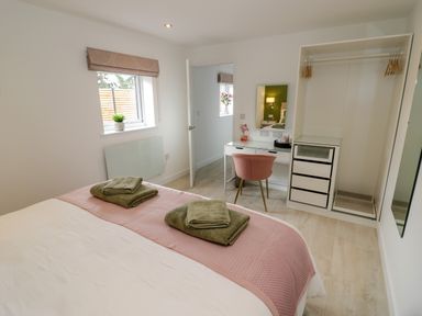 A bedroom with a bed covered with a pink blanket and green towels open closet a white desk with a mirror and a pink chair at The Croft in Shipston-On-Stour