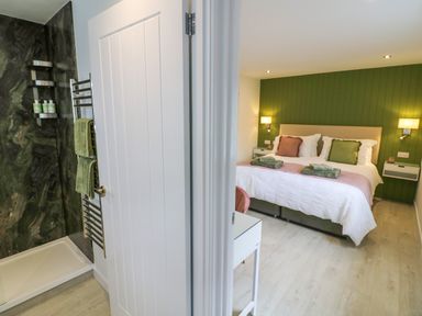 A bathroom with a shower and towel rack next to a bedroom with a double bed green accent wall and bedside tables at The Croft in Shipston-On-Stour