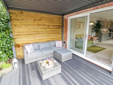 An outdoor patio with a gray wicker sectional sofa and a matching coffee table next to sliding glass doors leading to a living area at The Croft in Shipston-On-Stour