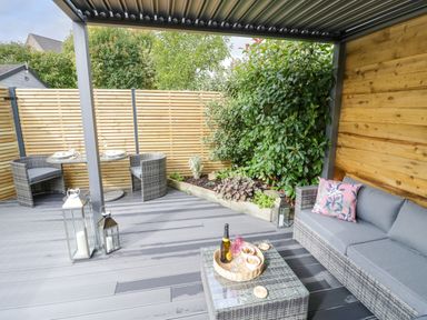 A covered outdoor patio with wicker furniture a small dining table and plants at The Croft in Shipston-On-Stour