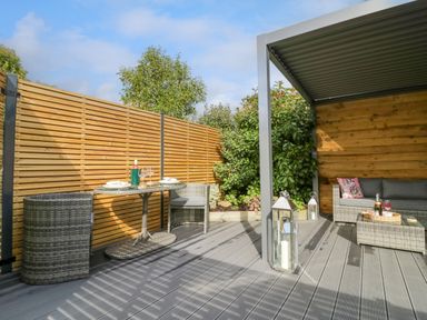 An outdoor patio area with wicker chairs table and a sofa under a metal pergola at The Croft in Shipston-On-Stour