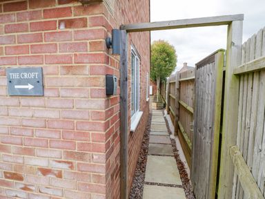 A narrow outdoor pathway with paving stones between a brick building and a wooden fence at The Croft in Shipston-On-Stour