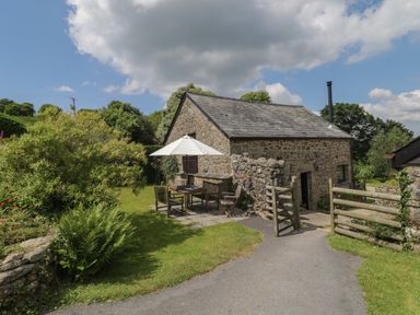 A stone cottage with outdoor wooden furniture and umbrella in a garden at Beckaford Cottage in Bovey Tracey