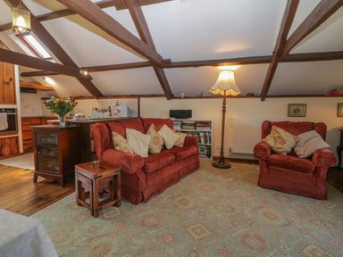 A living room with red upholstered sofa and armchair near wooden beams and a floor lamp at Beckaford Cottage in Bovey Tracey