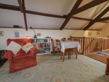 A sitting area with a red armchair, a bookshelf, and a dining table with four chairs at Beckaford Cottage in Bovey Tracey