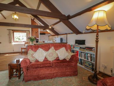 A living room with a red sofa and patterned cushions next to a bookshelf and a floor lamp at Beckaford Cottage in Bovey Tracey